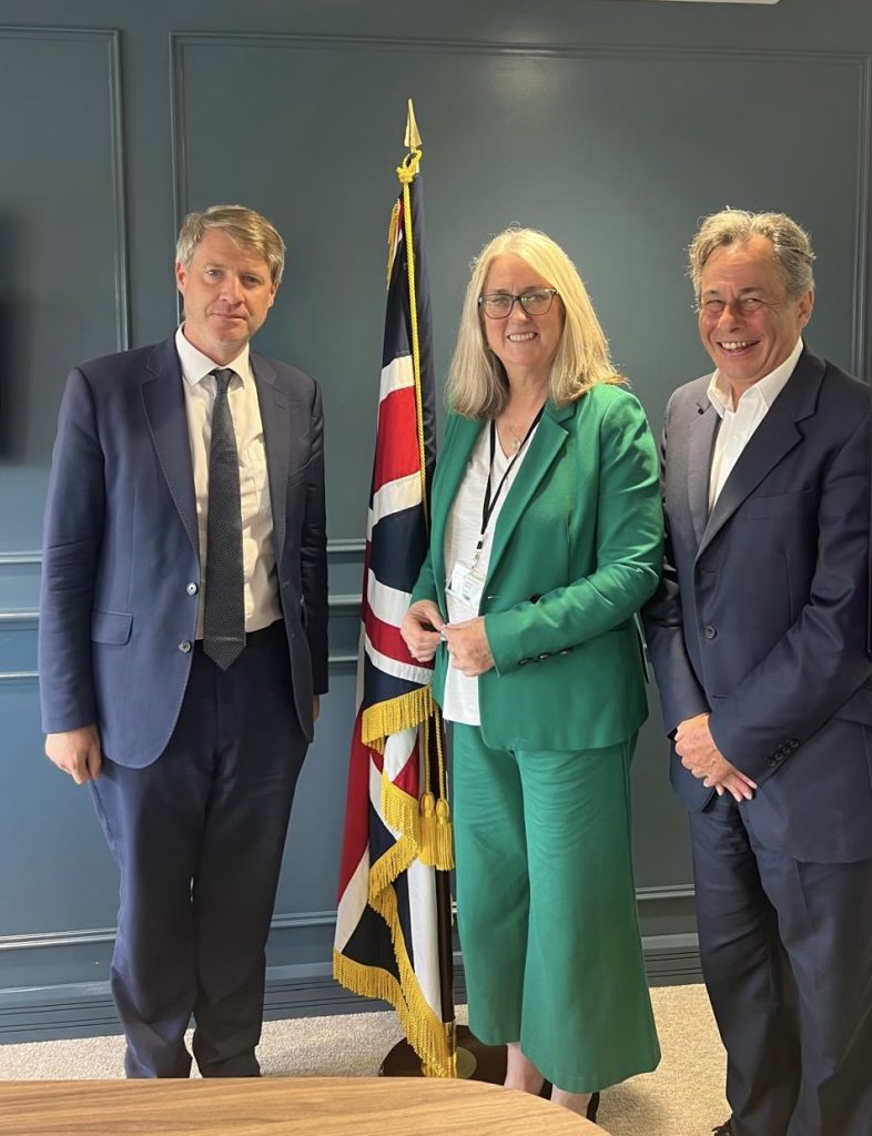 A photograph of Chris Skidmore, Jacqui Smith and David Pilsbury smiling, standing in front of a British flag.